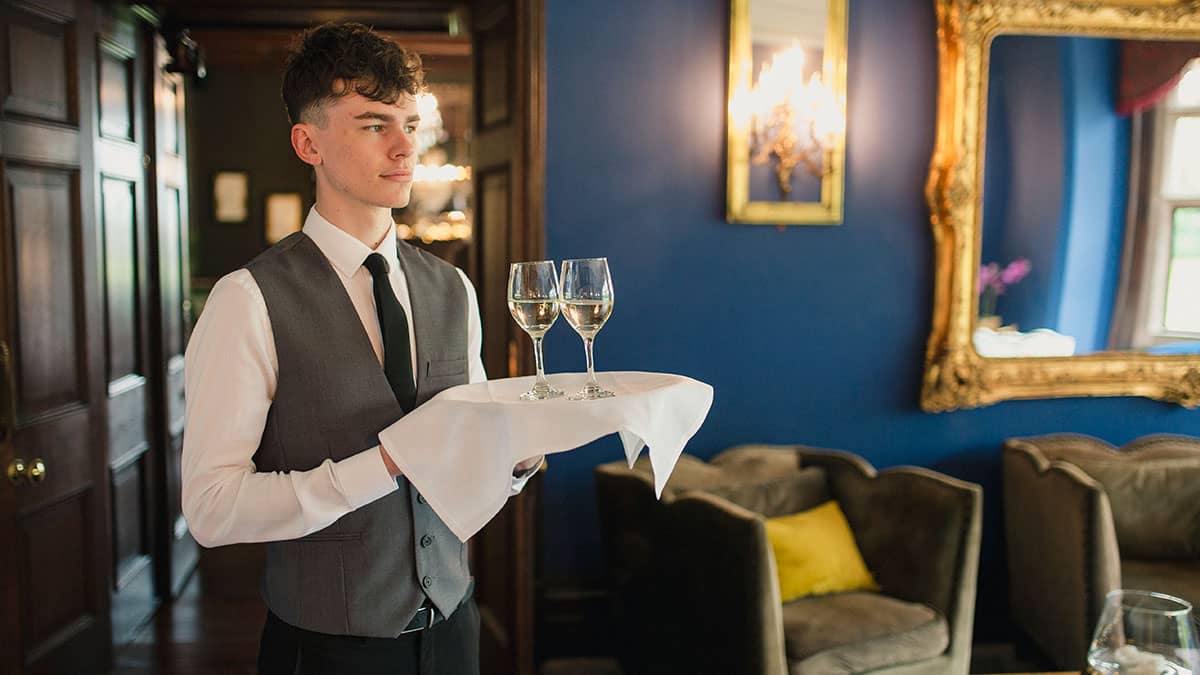 Male waiter carrying tray with two glasses filled with white wine 