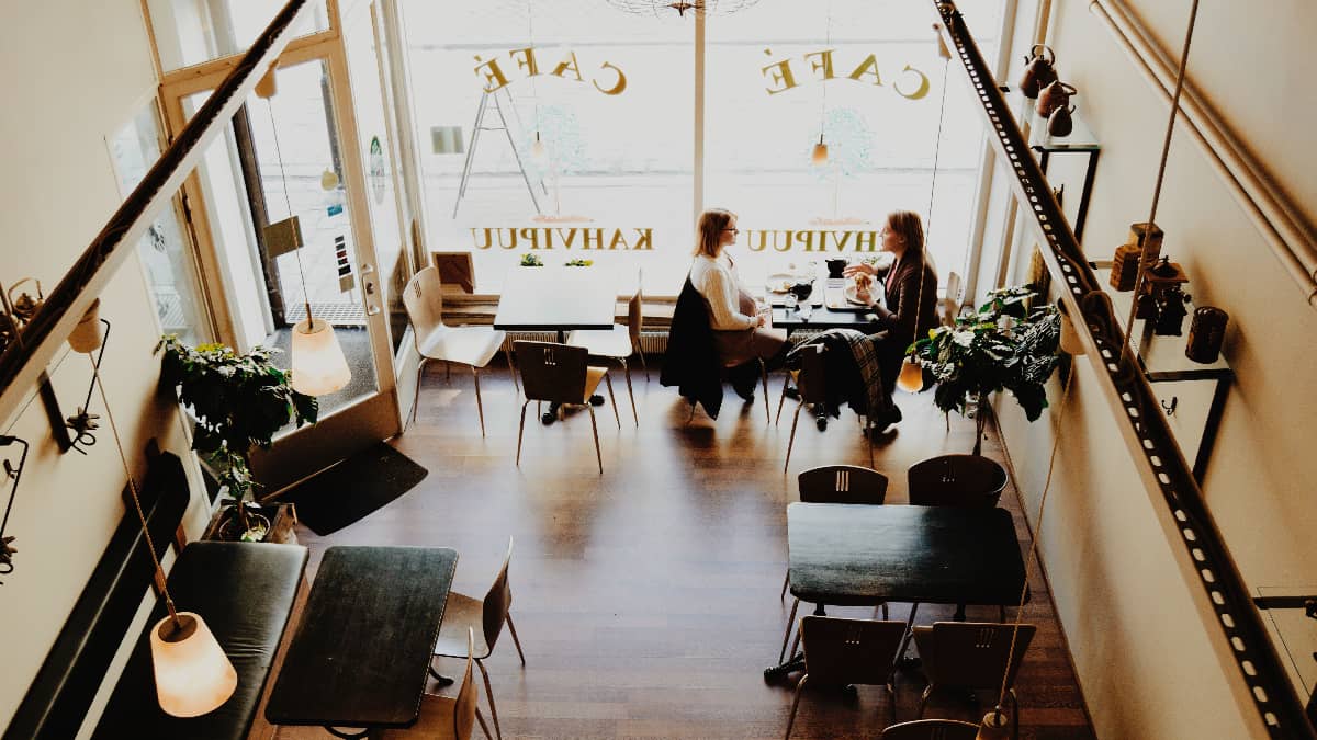 Two people at a table in a cafe talking, sat by the window.