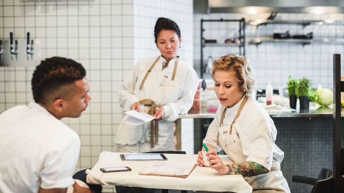 Three chefs in a kitchen having a meeting at a table. 