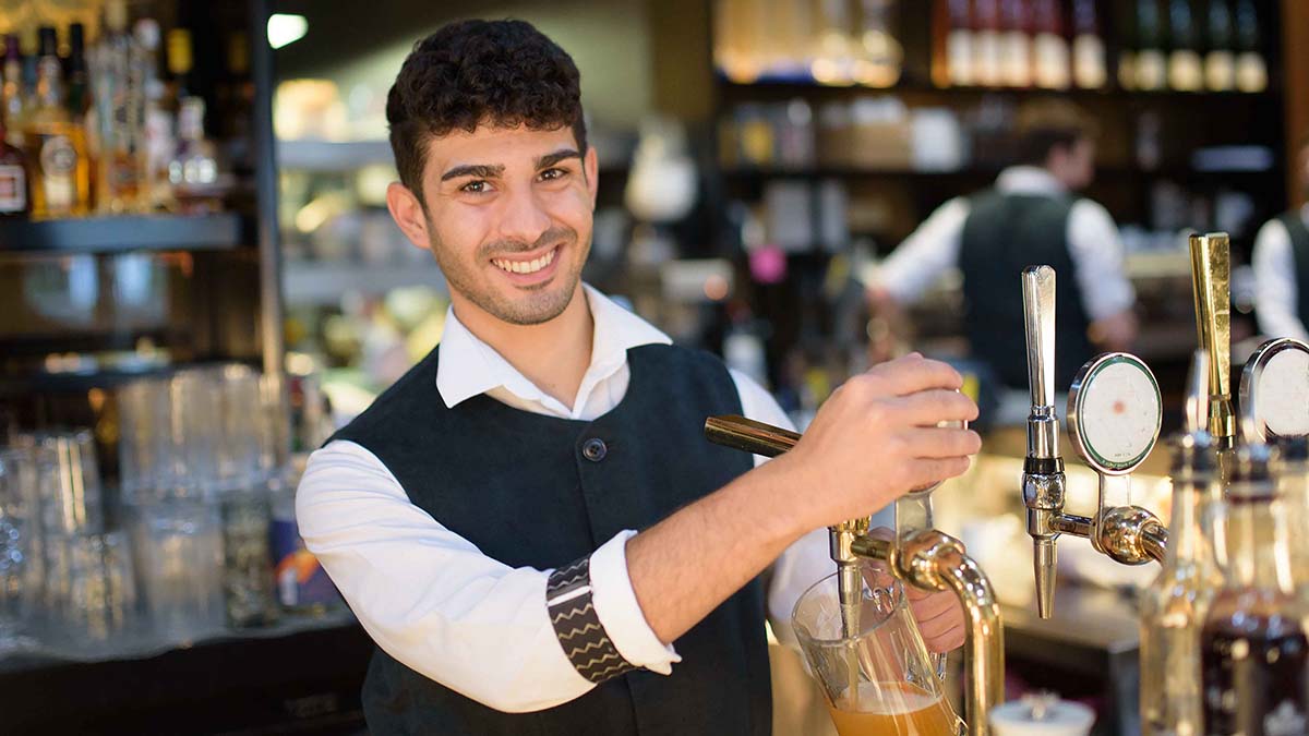 A happy barman, smiling and pulling a pint at a bar