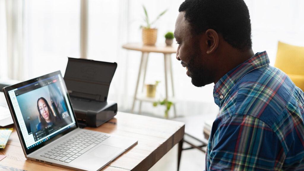 A man on at a desk with an open laptop on a  video call with a woman